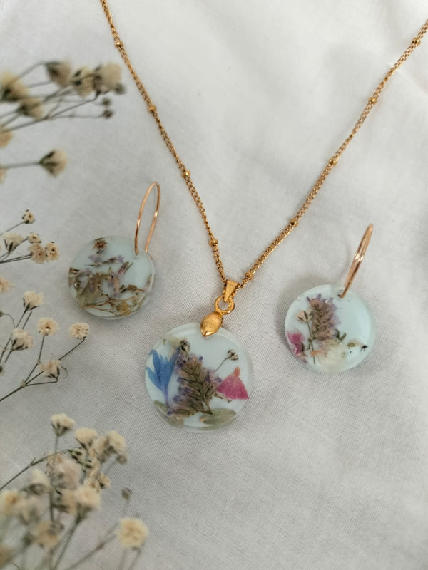 Juego dije y aretes circulo con flores preservadas y encapsuladas con resina epòxica y cadena de acero inoxidable